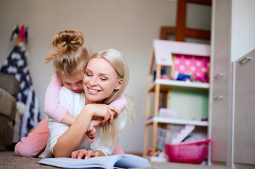 Young mother is relaxing and having fun at home with her daughter, a woman is reading a book to her child, a strong family, love, concept.