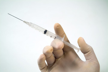 A hand with a surgical glove holds an medical injection.