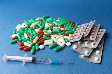 many multi-colored medical antiviral pills with syringe on blue background close-up