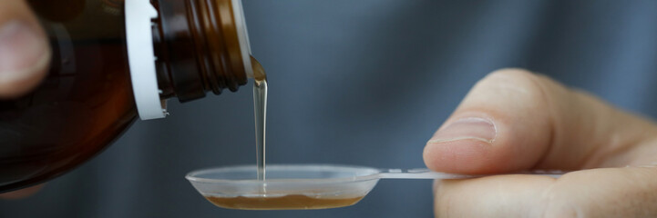 Close-up of male hands holding holding bottle of cough expectorant syrup and pouring it with...