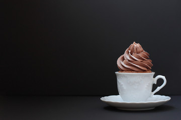 A chocolate cupcake in a small ceramic white coffee cup. Black background