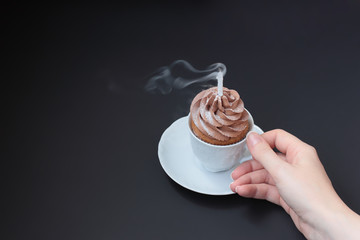 A chocolate cupcake in a small ceramic white coffee cup with a extinguished smoking candle. Black...