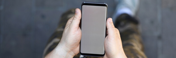 Top view of modern smartphone in male hands. Man in casual clothes holding stylish mobile phone. Empty copy space on gadget display. Blurred background