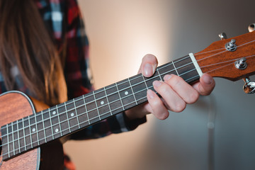 Fototapeta premium Young girl with long hair in a red shirt plays on ukuded sitting at home.