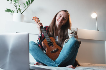 Girl sitting at home learns to play ukulele using online lessons.