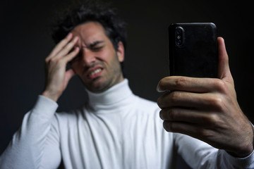 Close up of phone and handsome man with curly hair, he have headache, feel stressed and painful