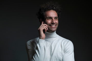 Portrait of handsome young male with curly hair, he holding his phone and feel so happy