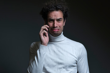 Portrait of casual man with curly hair, holding his phone, he is sad and crying