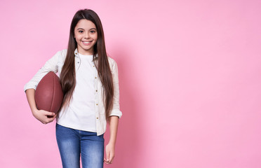 Graceful cute beautiful Caucasian girl with a ball for American football, in a white T-shirt on a pink background.