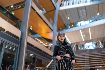 Young women in leatherjacket and striped pants posing in empty shopping mall