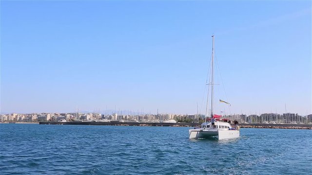 white catamaran emerges from the marina against the background of the city of Athens, Greece, crisis in Greece, yacht trip, sea ped Athens