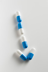Several blue and white capsules over a white surface arranged in an arrow shape.