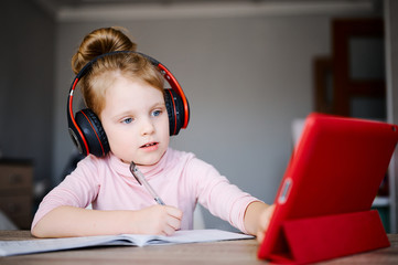 Distance learning online education. Schoolgirl in headphones studying at home with digital tablet and doing school homework. Training books and notebooks on table