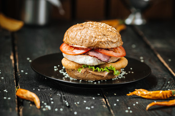 Big burger on black plate dark wooden background - obrazy, fototapety, plakaty