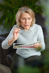 news, press, media, holidays and people concept - woman reading newspaper at home