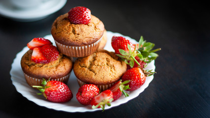 Homemade muffins with fresh strawberries on white plate on black table. Homemade tasty dessert or breakfast. Healthy eating concept