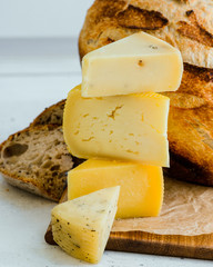 Stack of assorted cheeses and craft bread on wood board