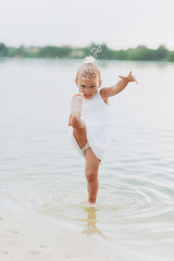 Naklejka premium cute baby girl walking and having fun on the beach near lake. The concept of summer holiday. baby's day. Family spending time together on nature.