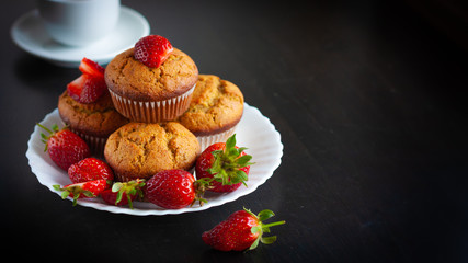Homemade muffins with fresh strawberries on white plate on black table. Homemade tasty dessert or breakfast. Healthy eating concept