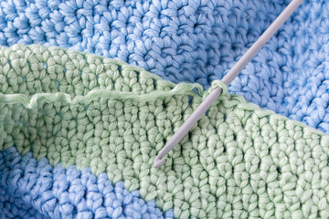 Crochet hobby background with hook. Close up. Crochet process. Green and blue almost finished plaid.