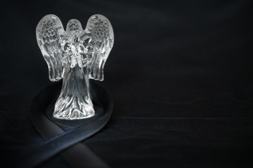 Crystal angel statuette on a black background with a funeral ribbon: space for text