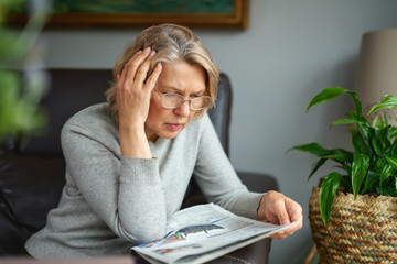 news, press, media, holidays and people concept - woman reading newspaper at home