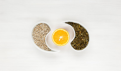 Pumpkin and sunflower seeds lie on a white background with garlic cloves in the form of a Yin-Yang sign, with an orange cut between them. Concept of healthy food, organic food. The view from the top.