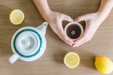 Femme tenant une tasse de thé au citron sur une table en bois et faisant un coeur avec ses mains
