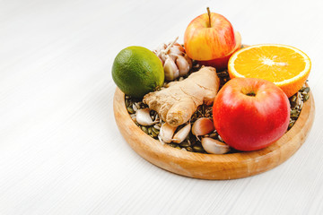 Orange, ginger, garlic, lime, lemon, sunflower seeds, Apple, pumpkin seeds lie on a round wooden plate on a white wooden background. Organic healthy, immune natural products, side view.