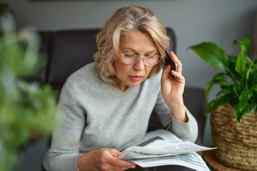 Adult woman reading newspaper with phone in hands.News, press, media, holidays and people concept .