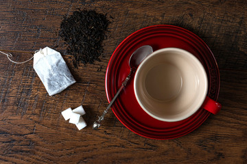 Tea cup with tea bag, cookie, sugar cubes, teaspoon, loose tea, on wood background