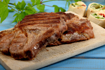 two pieces of grilled meat on a cooking plate with pieces of tortilla next to a cold drink on an old blue table