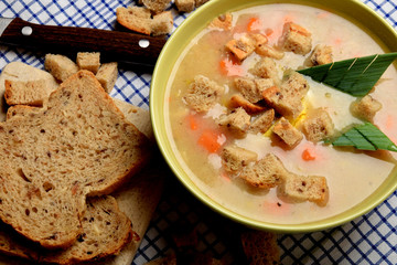 Vegetable soup with sausage and pieces of bread on a blue checkered napkin