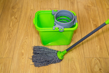 MOP with bucket for rinsing and wringing water green on a background of brown laminate, care...