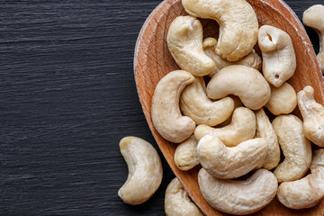 Wooden bowl of cashew nuts from above on black background. Top view, copy space for text. Healthy snack, vegetarian food, beer snack