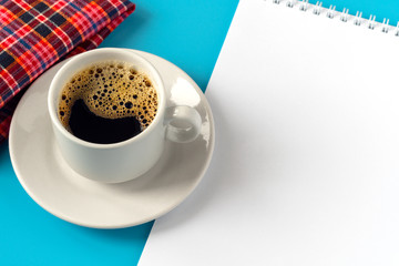 notebook with white workspace for inscriptions next to a cup of coffee and a red napkin on a blue background
