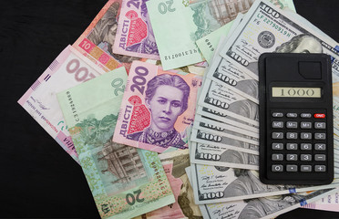 different hryvnias, dollars and calculator on a black background. View from above. Business horsepower. The concept of the growth or fall of the hryvnia.