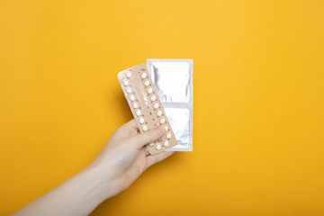 The girl holds contraceptive pills and condoms in her hands. Contraception. Yellow background place for text.