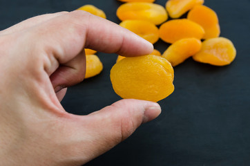 ripe dried apricots in a female hand on a background of dried apricots. Black background. Close-up.
