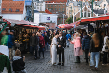 Lovers stand in the middle of a crowd of blurry walking people at a market in Bergen