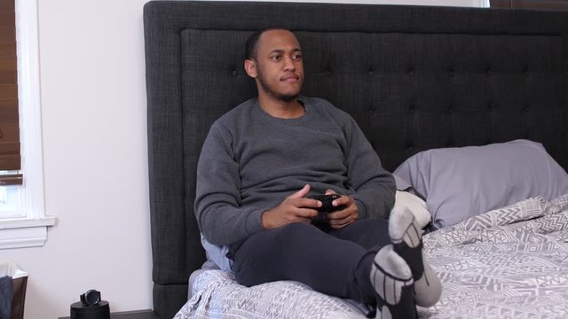 Black man playing with controller in bed