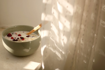 Breakfast bowl with oatmeal, berries and coconut chips, illuminated by morning sunlight. Selective focus.