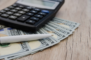 dollars, pen and calculator on a wooden background.