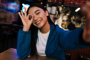 Photo of joyful nice asian woman gesturing ok sign while taking selfie