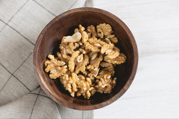 Wooden bowl full of walnuts on a gray napkin.