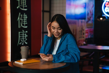 Fototapeta na wymiar Photo of asian woman using mobile phone while sitting in cafe