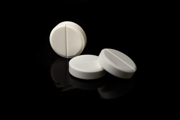 White pills are on a black table with a reflective surface.