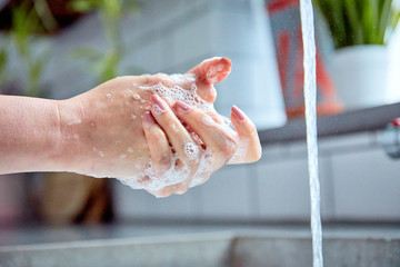Washing hands. This is an example of a woman thoroughly washing her hands, with a tap running, showing really good, clean hands. This image has plants in the background, and shot with natural light