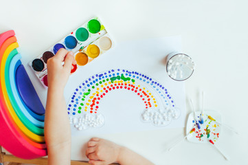 Kids hands painting dot rainbow using cotton sticks on white background