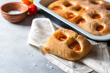 Italian bread focaccia with tomatoes and sea salt on grey concrete background. Homemade baking.